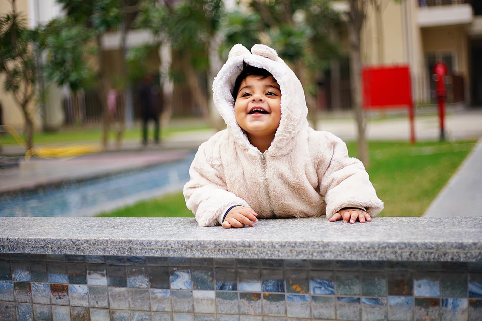 Child in a fluffy white hooded jacket leaning on a tiled ledge